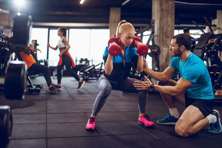 Personlig tränare hjälper kvinna med träning i ett gym.